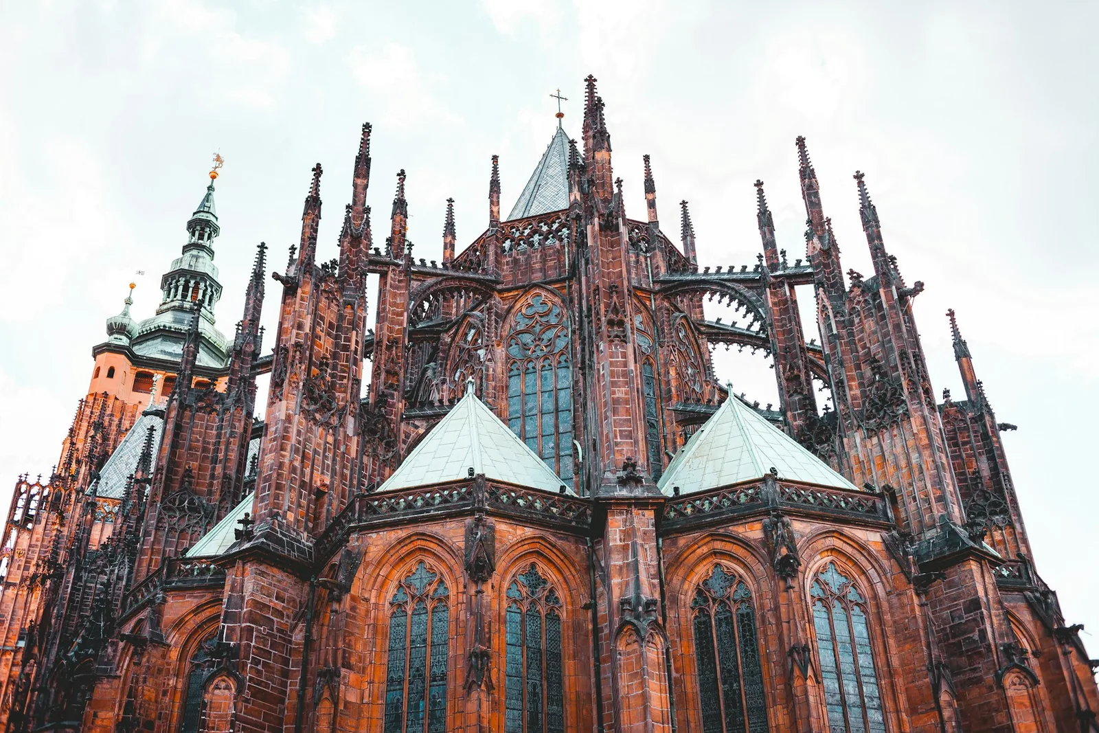 The Gothic spires and flying buttresses of St. Vitus Cathedral within Prague Castle, seen from below against a pale sky