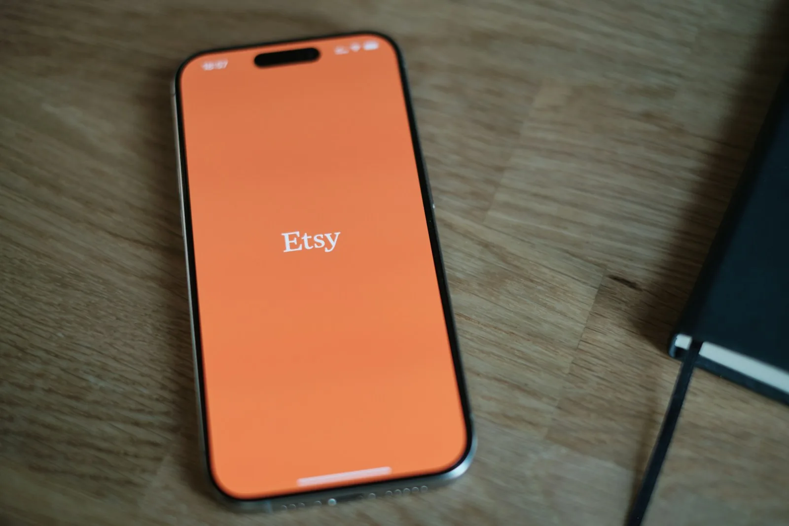 A smartphone on a wooden desk showing the Etsy app opening screen