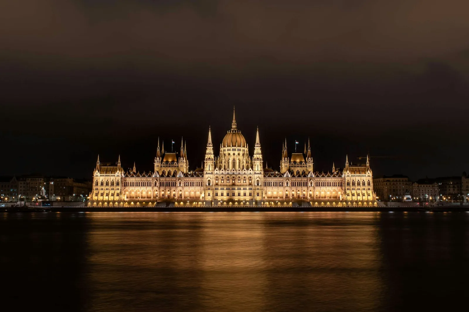 The Hungarian Parliament Building illuminated at night, its Gothic Revival dome and spires reflected in the Danube