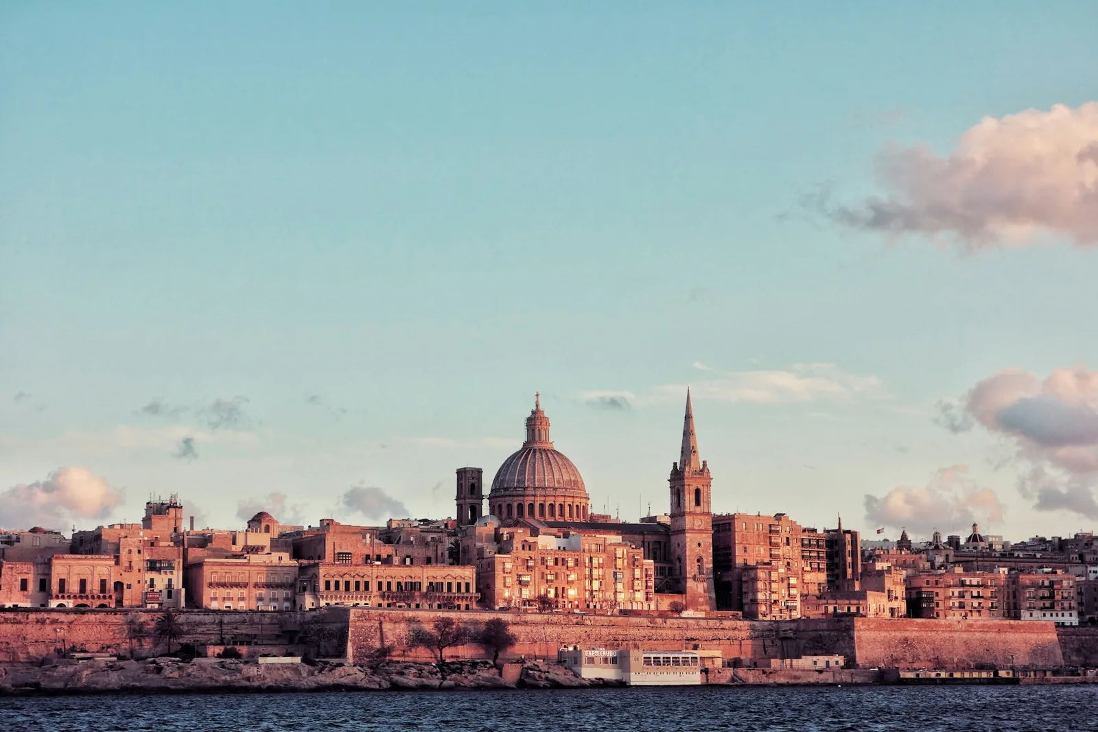 The Valletta skyline at sunset across the harbour, the dome of the Carmelite Church and St. Paul's Cathedral spire rising above the fortified city
