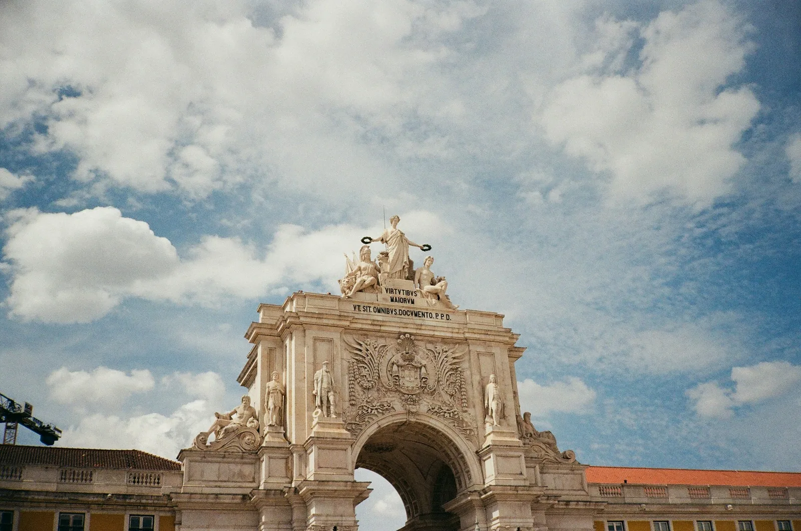 The triumphal Arco da Rua Augusta in Lisbon, its stone archway crowned with allegorical statues against a blue sky