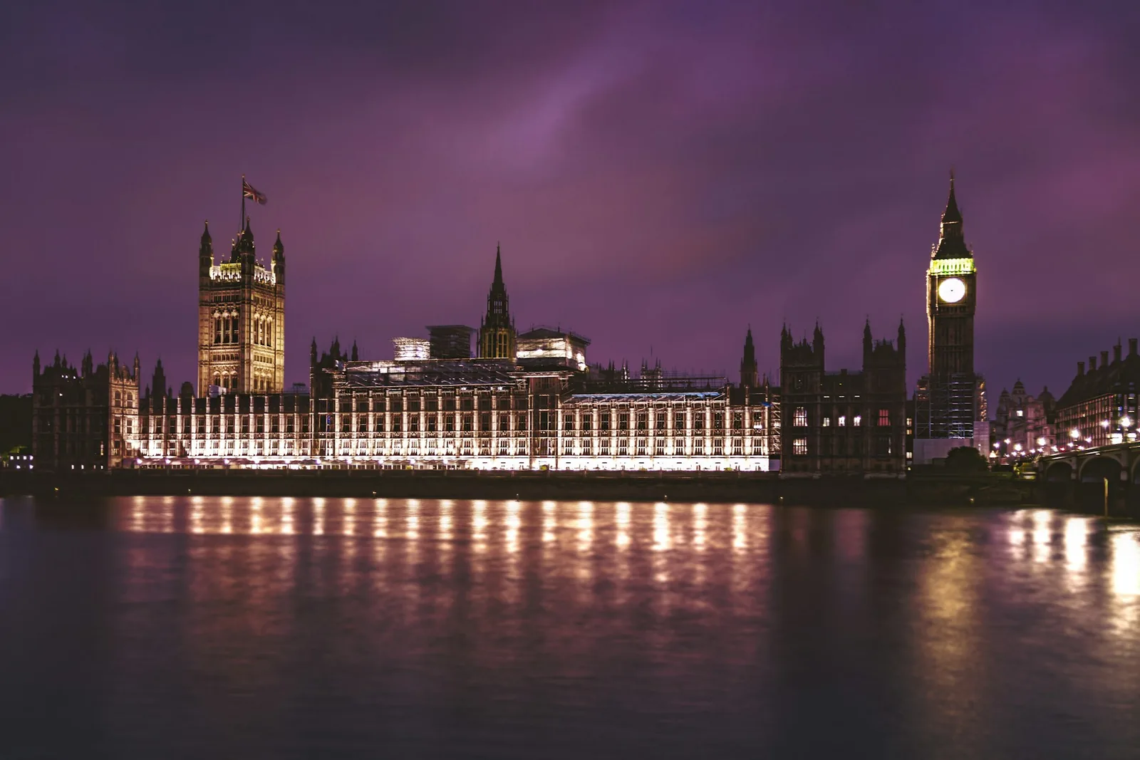 The Houses of Parliament and Big Ben lit up on the Thames at dusk under a dramatic purple sky