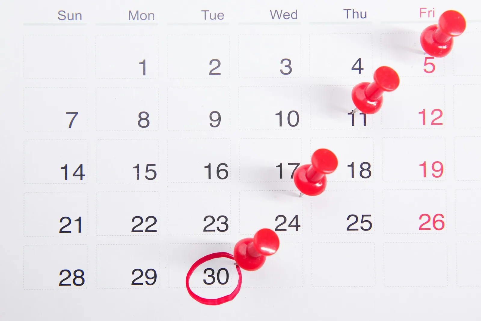 A wall calendar with red pins marking dates and the 30th circled in red