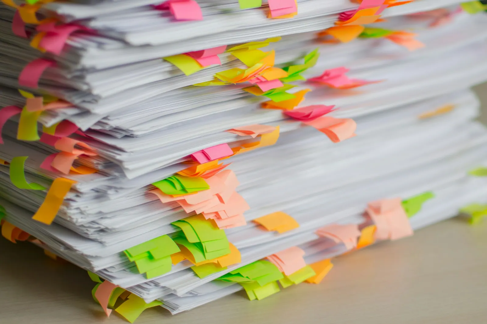 A tall stack of paper filings flagged with colourful sticky tabs, evoking the many separate EPR registrations a seller must track