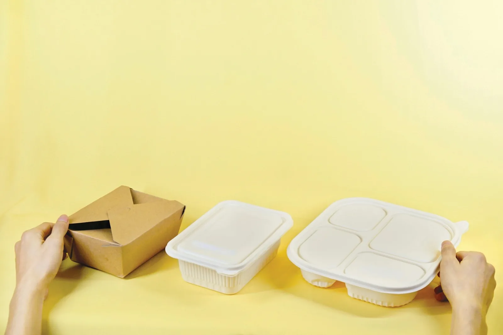 Hands arranging paper and fibre takeaway food containers on a yellow surface
