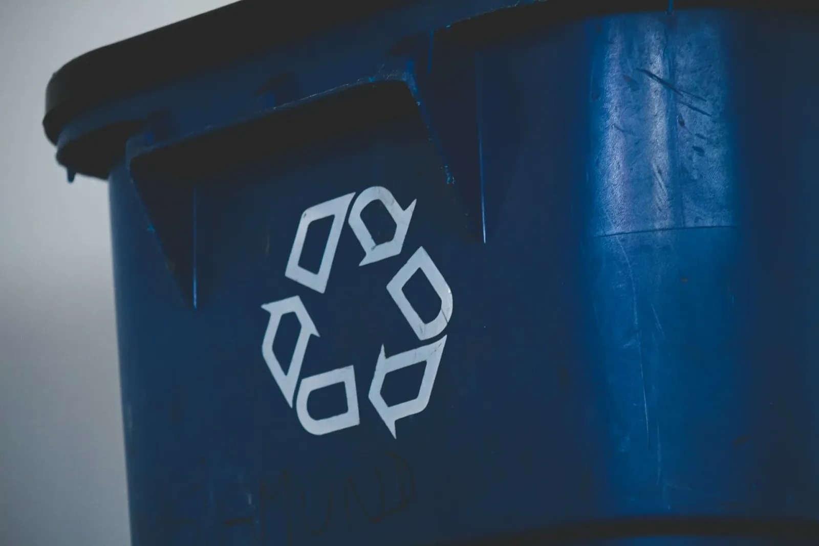 White recycling symbol on the side of a blue plastic recycling bin