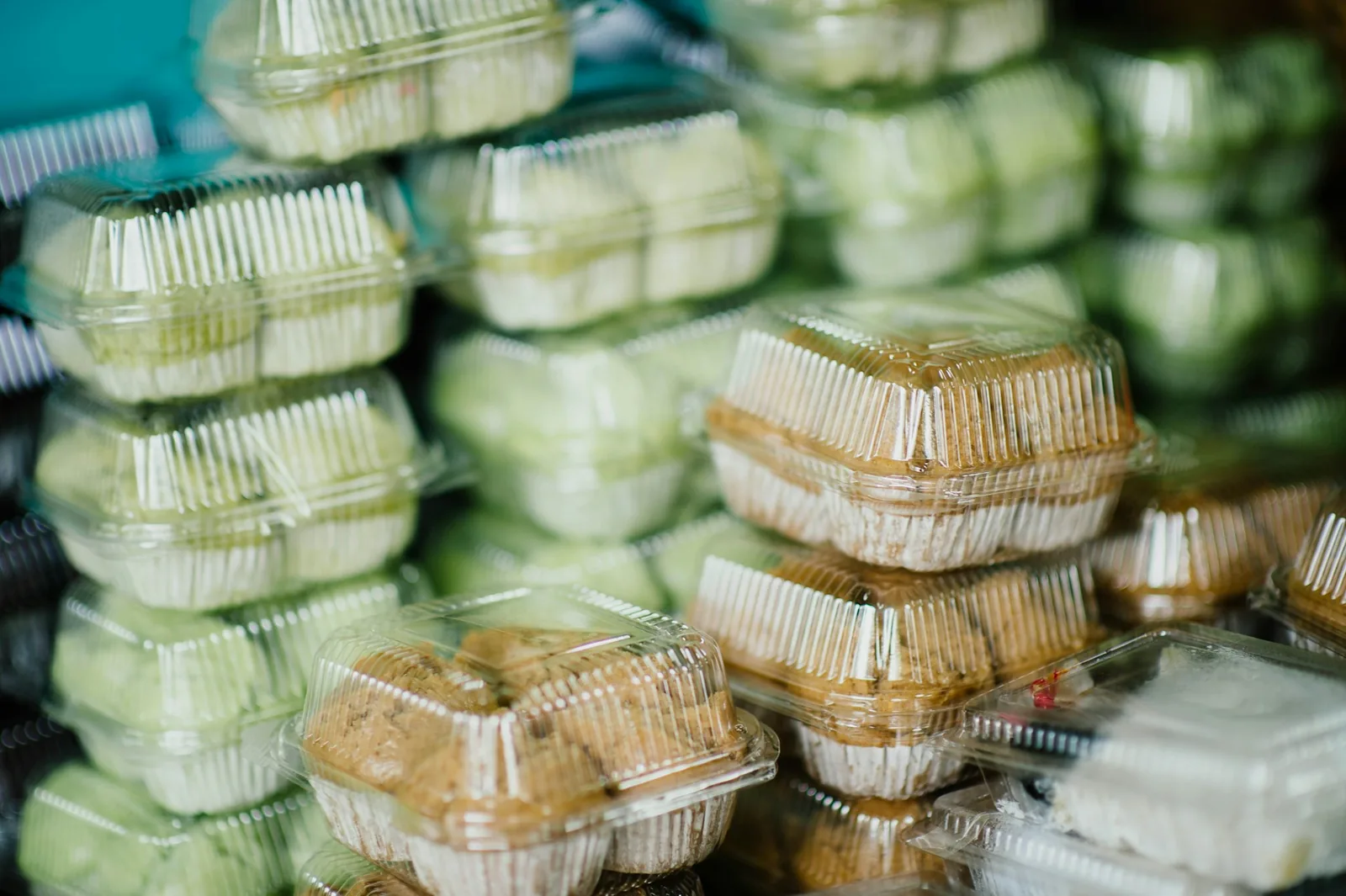 Stacks of clear single-use plastic clamshell food containers filled with baked goods