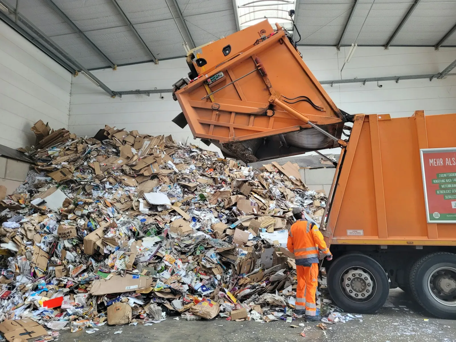 Refuse truck tipping a large pile of cardboard and paper packaging waste at a recycling sorting facility
