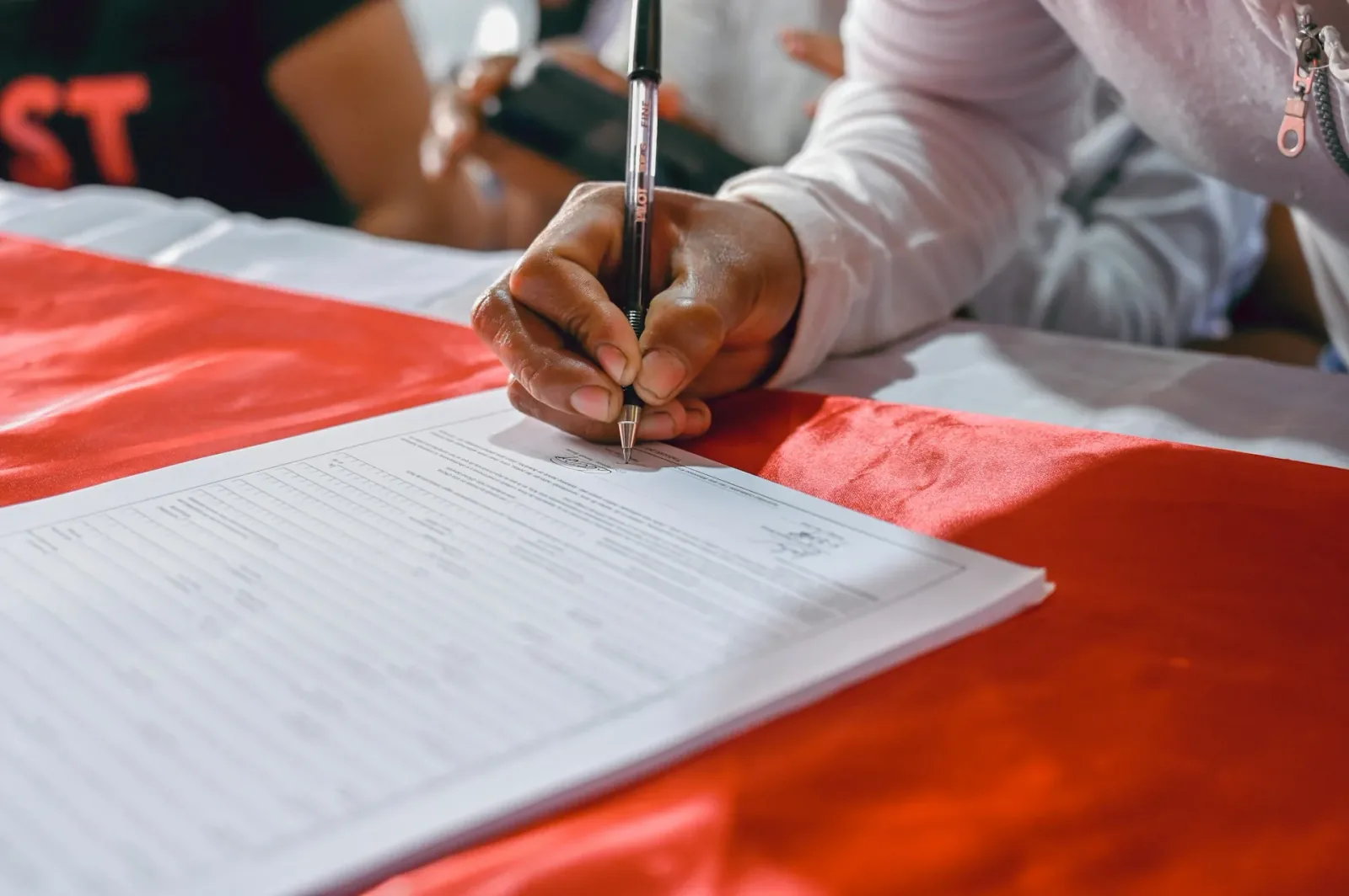 Person signing a printed registration form with a pen